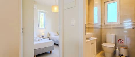 A hotel room with a bed, bedside table, lamp, and a view of the bathroom.
