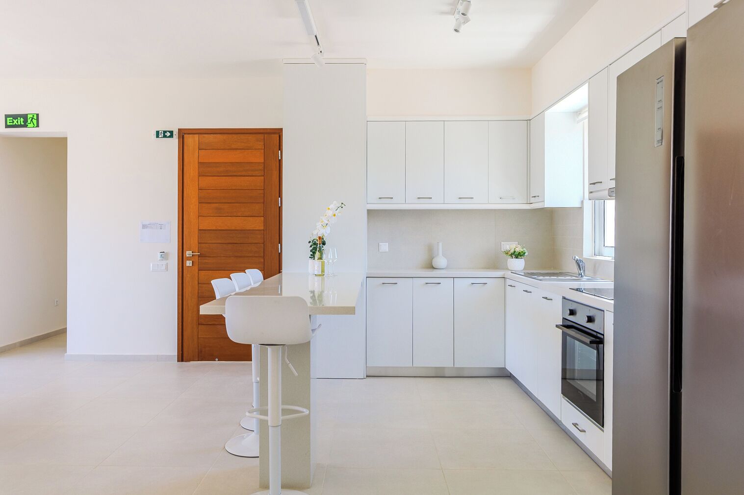 A modern kitchen with white cabinets, a stainless steel refrigerator, and a wooden door.