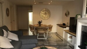 A modern living room with a grey sofa, a round coffee table, and a dining area with wicker chairs and a central table. - Monte Duquesa, ground floor, 2 bed close to Port and Beach (Manilva)