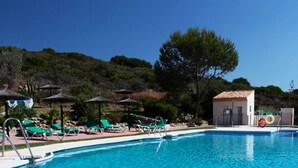 A pool area with lounge chairs, umbrellas, and a small building, surrounded by trees and hills. - Monte Duquesa, ground floor, 2 bed close to Port and Beach (Manilva)