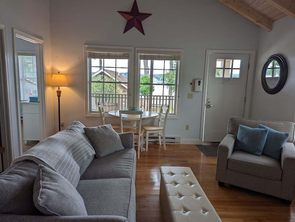 A living room with a gray sofa, a beige ottoman, and a gray armchair. There is a star decoration on the wall, a lamp, and a door with a mirror.