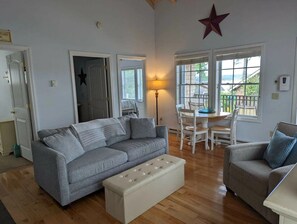 A living room with a grey sofa, a white ottoman, a dining table with chairs, and a star decoration on the wall.