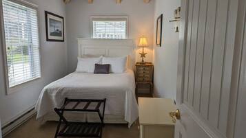 A bedroom with a bed, a nightstand with a lamp, a bench, and a window.