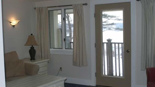 Una habitación con cama, una mesita de noche con lámpara, una ventana con cortinas y vistas a un paisaje nevado.