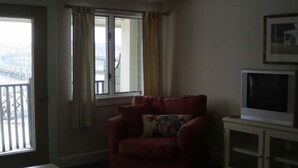 Una sala de estar con un sofá rojo, un televisor sobre un mueble bajo y una ventana con cortinas.