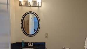 Un baño con un espejo redondo, un lavabo con encimera negra, un inodoro y un cubo de basura.