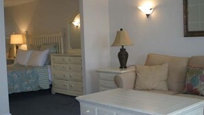 Un dormitorio con cama, cómoda, mesita de noche con lámpara y sofá.