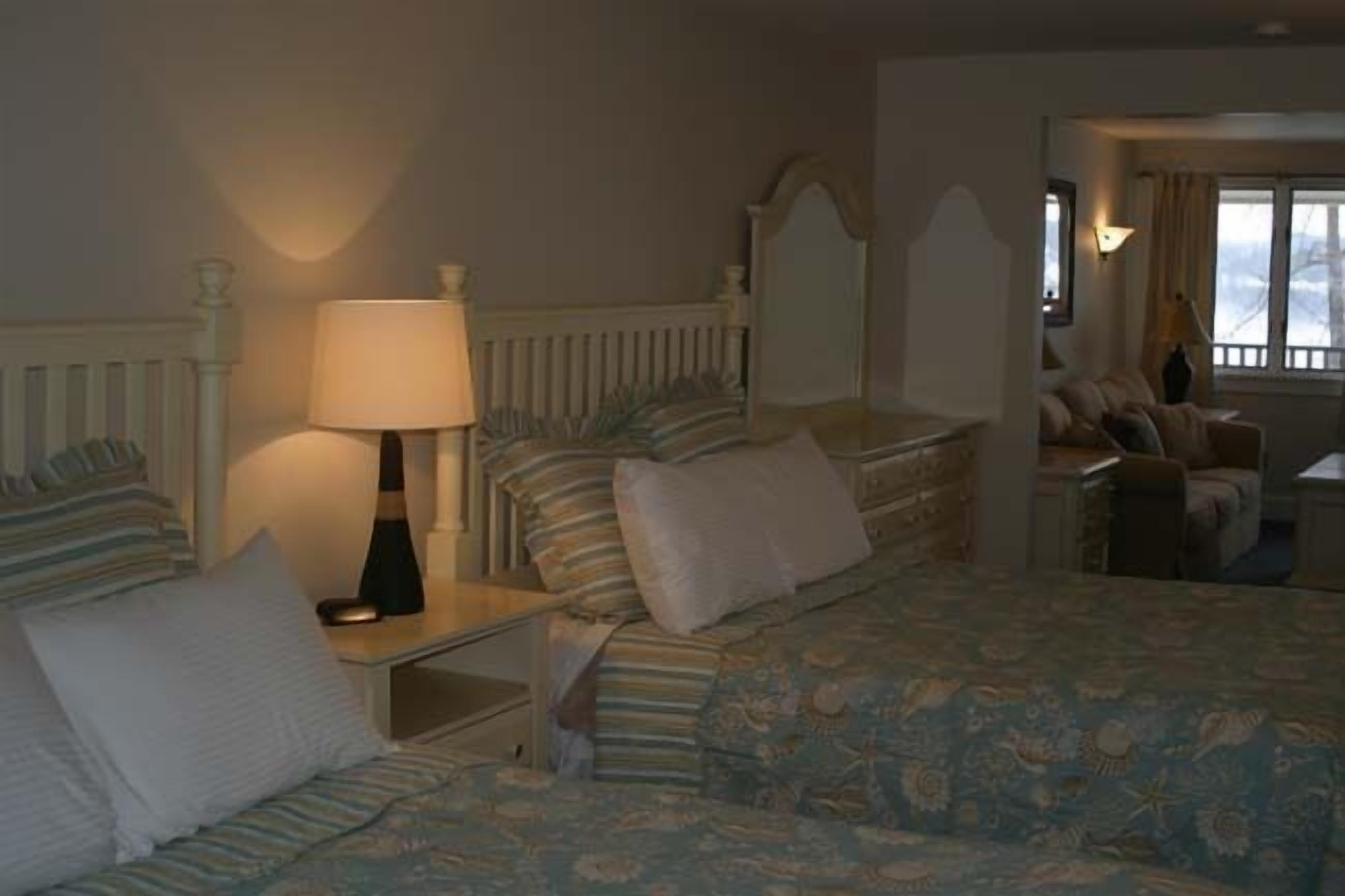 A hotel room with two beds, a nightstand with a lamp, a dresser, and a window with curtains.
