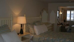 Una habitación de hotel con dos camas, una mesita de noche con lámpara, un aparador y un ventanal con cortinas.