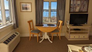 Ett rum med ett matbord, två stolar, en tv och utsikt över havet.