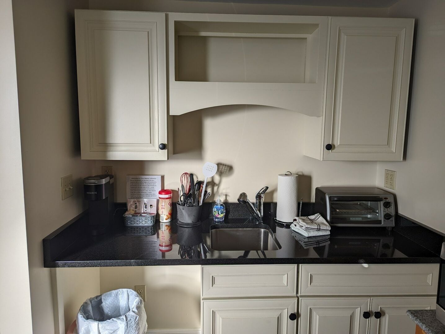 A kitchen with white cabinets, a black countertop, a toaster, and various kitchen utensils.