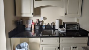 Ett kök med vita skåp, en svart bänkskiva, en kaffemaskin från Keurig, en brödrost och en papperskorg.
