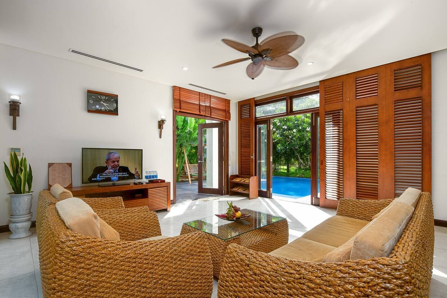 Una sala moderna con muebles de mimbre, un televisor y vistas a una piscina.