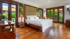 A spacious bedroom with a large bed, wooden flooring, a desk with a lamp, and large windows offering a view of greenery. - Luxury Pool Villas in Purama Villas (Da Nang)