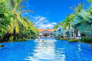 A swimming pool with palm trees, lounge chairs, and a building in the background. - Luxury Pool Villas in Purama Villas (Da Nang)