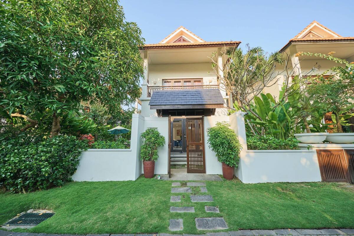 A two-story house with a tiled roof, a front door, and a small garden with a stone pathway leading to the entrance.