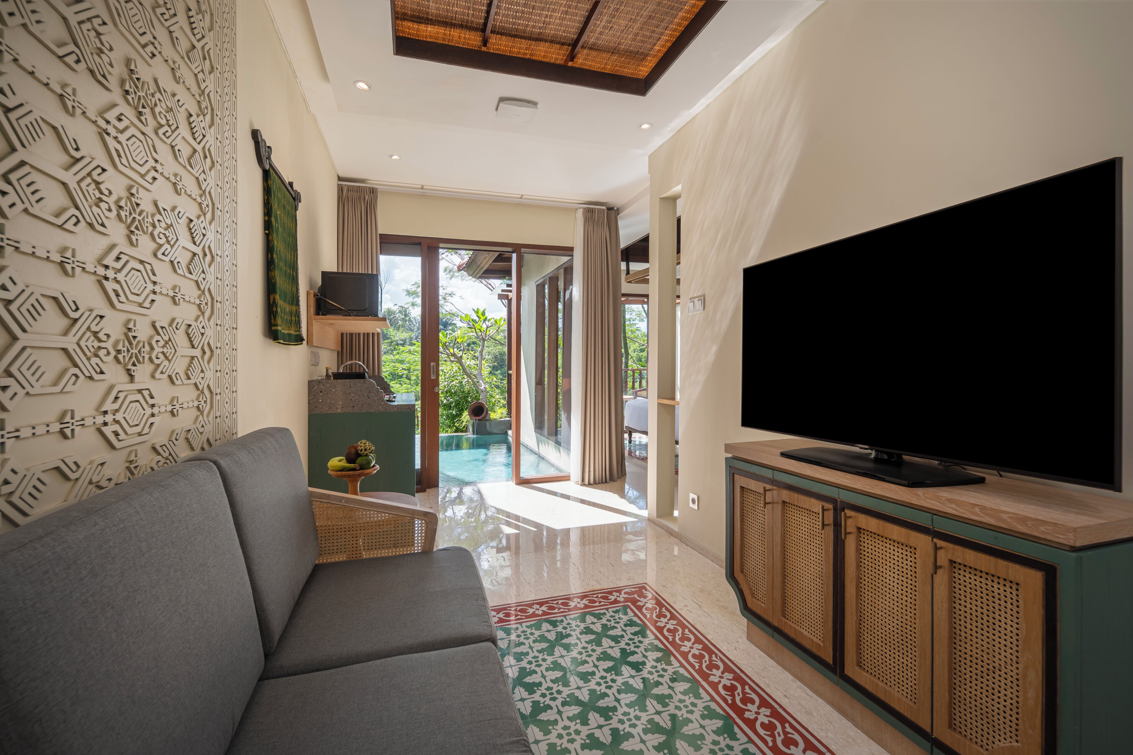 A modern living room with a grey sofa, a flat-screen TV on a wooden cabinet, and a patterned rug.