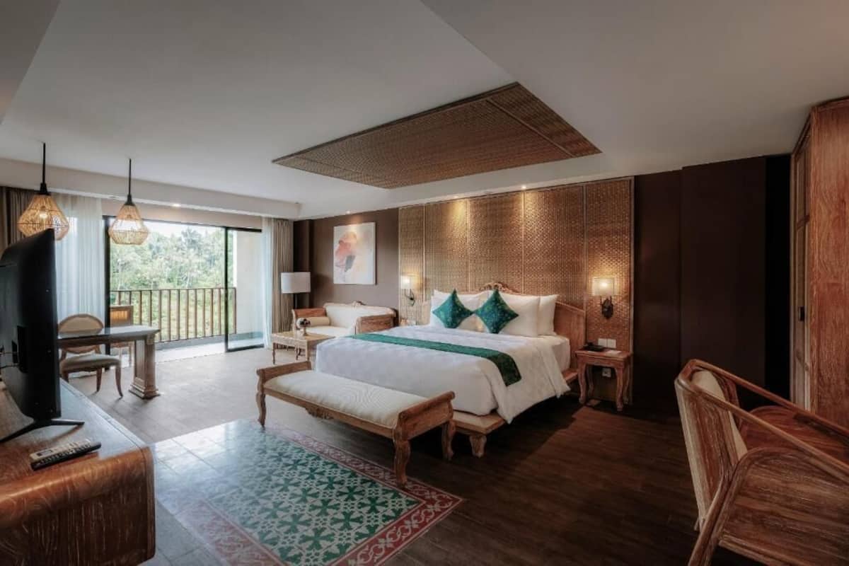 A spacious hotel room with a large bed, a desk, a chair, a TV, and a balcony.