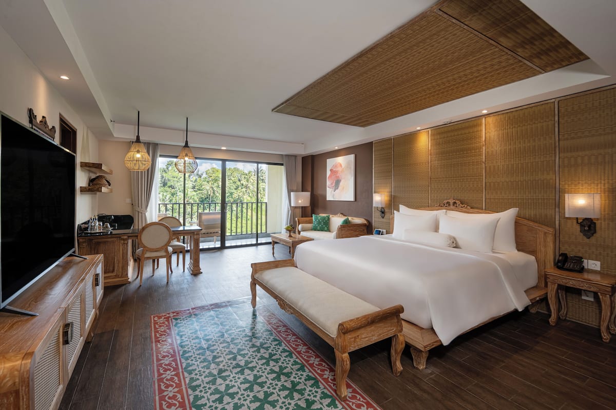 A spacious hotel room with a large bed, a TV, a dining area, and a balcony with a view.