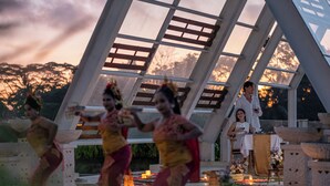 Un groupe de personnes exécutant une danse traditionnelle en plein air, avec une structure architecturale moderne en arrière-plan.