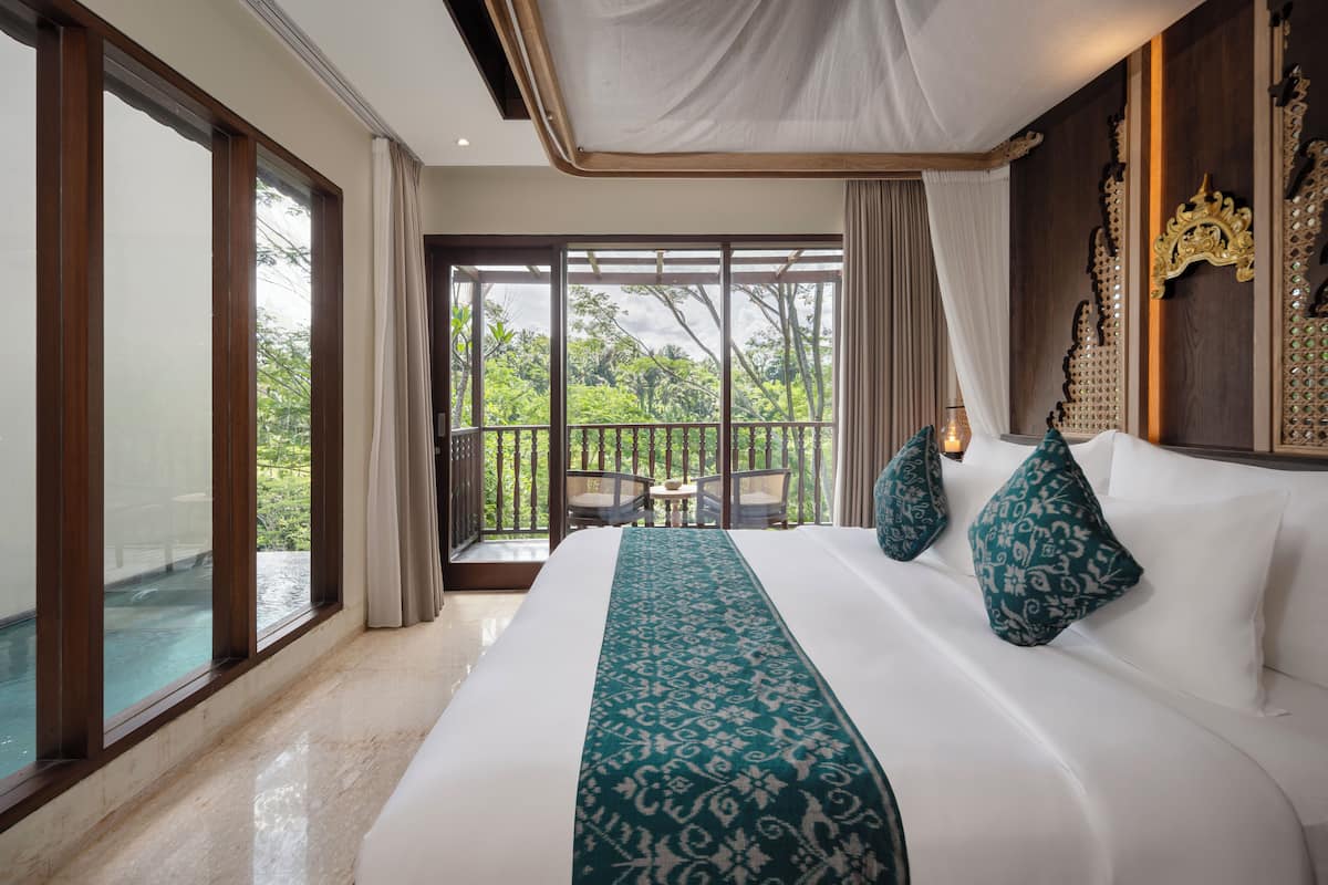 A spacious bedroom with a large bed, a balcony with a view of greenery, and a pool visible through the glass doors.