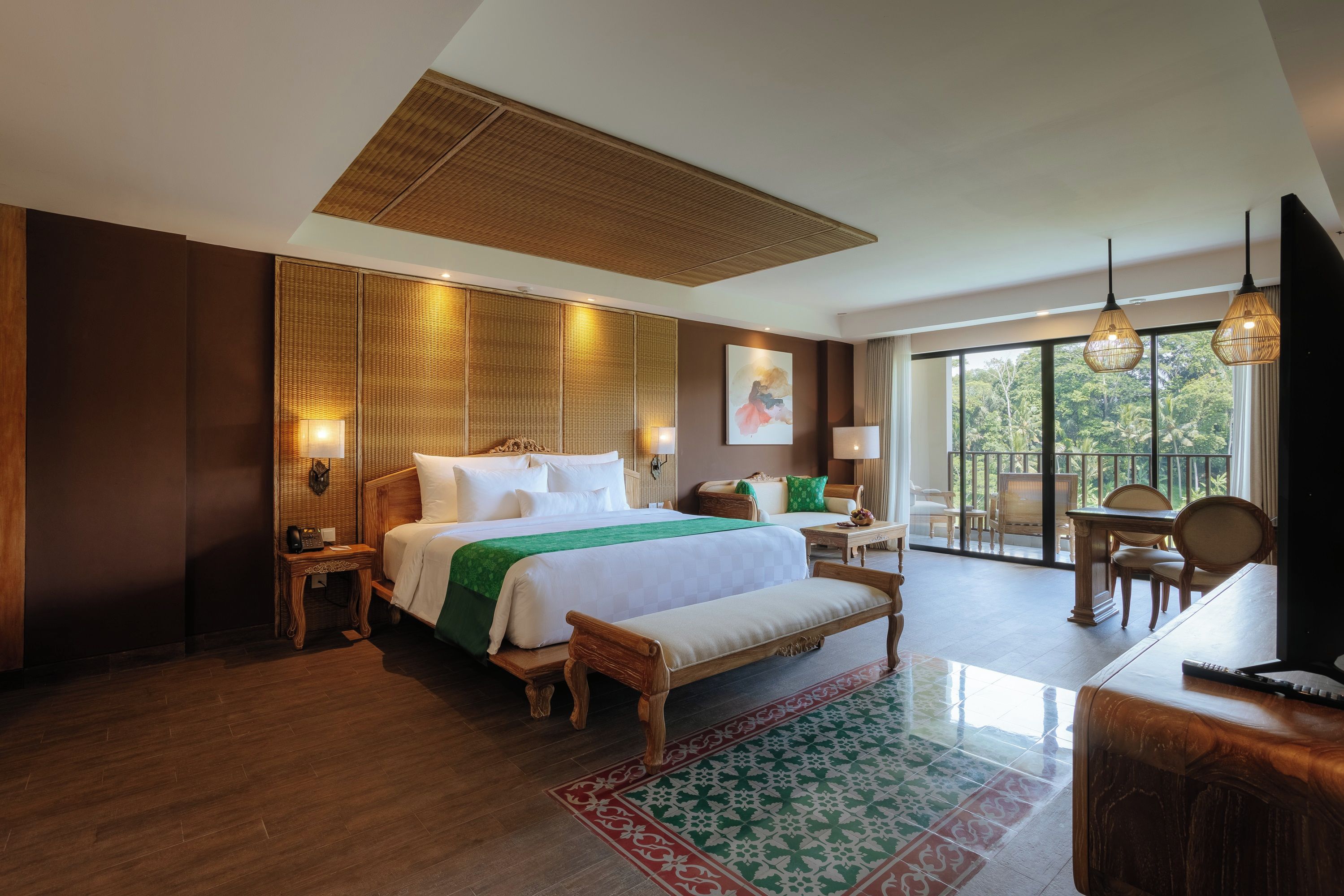 A hotel room with a large bed, bedside tables, a bench, a desk, and a TV.