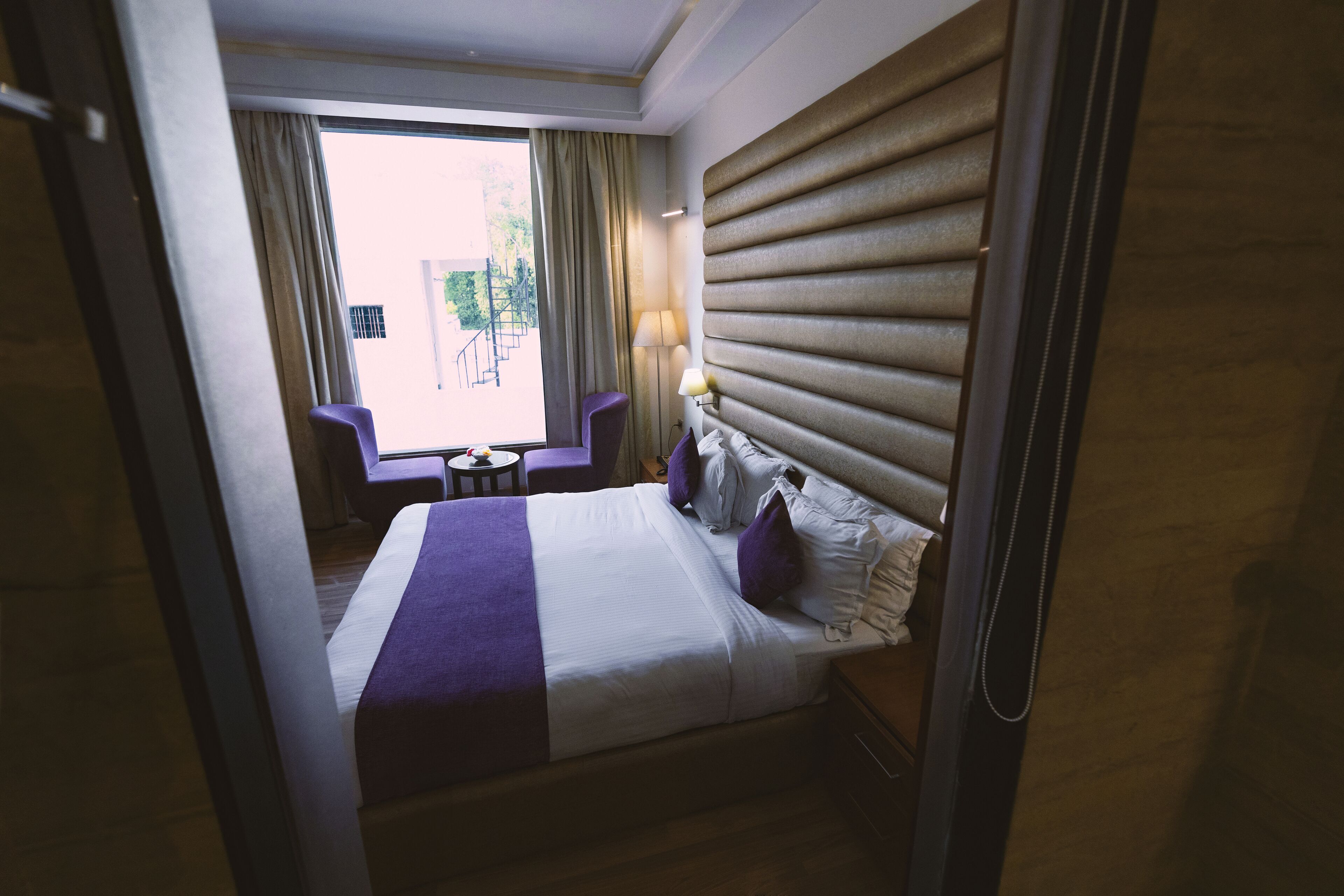 Una habitación de hotel con cama, escritorio, silla y ventana con cortinas.
