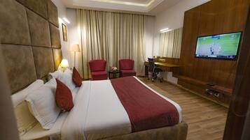Habitación de hotel con una cama grande, dos sillas rojas, un escritorio, un televisor y suelo de madera.