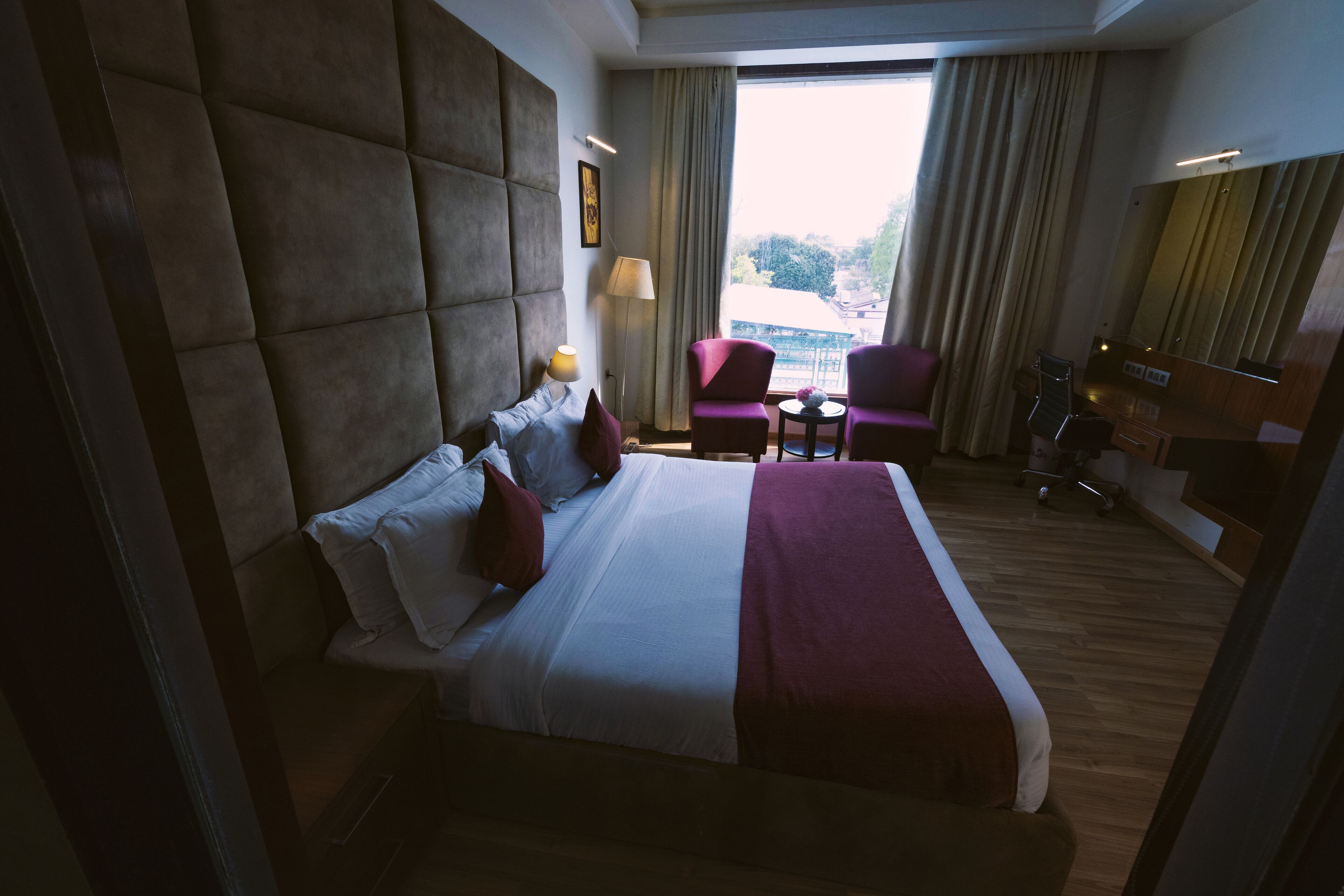 Une chambre d’hôtel avec un grand lit, un bureau, deux chaises, une petite table et une vue sur la ville par la fenêtre.