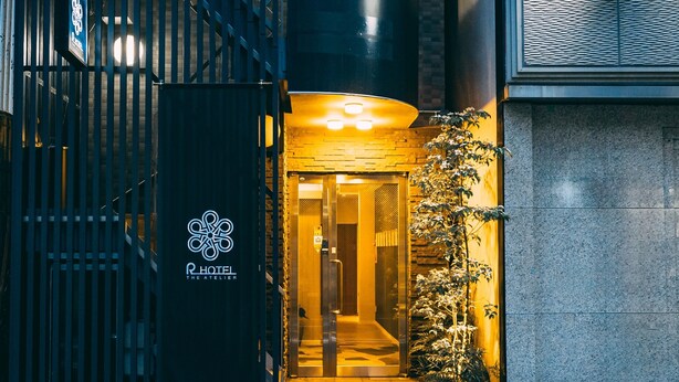 A hotel entrance with a black gate, a glass door, and a small plant beside it. - R Hotel-The Atelier Shinsaibashi East (Osaka)