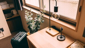 A hotel room with a wooden desk, a potted plant, a suitcase, a lamp, and a window with a view. - R Hotel-The Atelier Shinsaibashi East (Osaka)