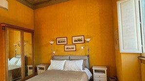 Ein Schlafzimmer mit einem großen Bett, einem Holzschrank, Nachttischen, gerahmten Bildern an der Wand und einem Fenster.