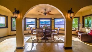 A dining area with a table and chairs, a ceiling fan, and large windows with a view of the ocean.
