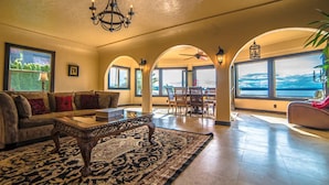 A spacious living room with a large sofa, a coffee table, and a patterned rug. There are multiple windows offering views of the outdoors.