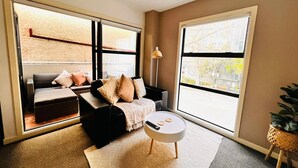 Un salon moderne avec un canapé noir, une table basse ronde et de grandes fenêtres donnant sur l’extérieur.
