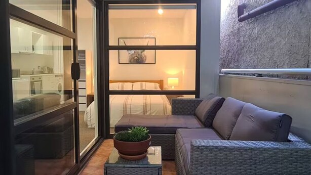 Une chambre à coucher de taille réduite, comprenant un lit, un petit coin salon et une plante en pot.