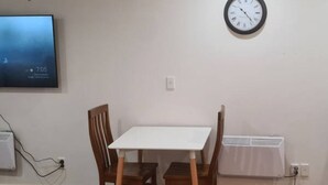 Une pièce avec une table blanche et deux chaises en bois, une horloge murale et un appareil de climatisation blanc.