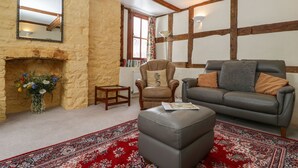 A cozy living room with a stone wall, a fireplace, a leather sofa, a wooden chair, and a patterned rug. - The Old Rectory (Presteigne)