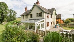 A two-story house with a conservatory, surrounded by a garden with various plants and a wooden fence. - The Old Rectory (Presteigne)