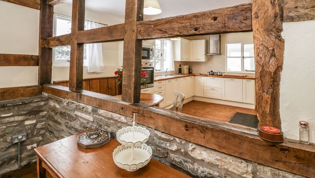 A rustic kitchen with exposed wooden beams, white cabinets, and a stone wall. - The Old Rectory (Presteigne)