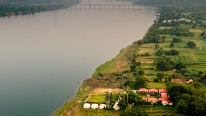 Vista aérea de una zona ribereña con un puente, campos verdes y edificios de tejados rojos.