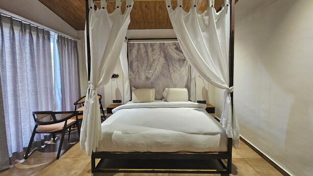 Una cama con dosel de madera, con sábanas blancas, techo de madera y un papel tapiz estampado detrás de la cama.