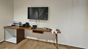 Una habitación de hotel con escritorio de madera, televisor de pantalla plana montado en la pared, teléfono y cafetera.