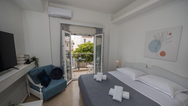 A modern hotel room with a bed, a sofa, a TV, and a balcony with a view of the city.