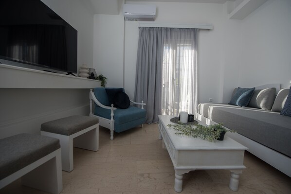 Una sala de estar moderna con un sillón azul, un sofá gris, una mesa de centro blanca y un banco blanco.