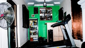 A room with a treadmill, a fan, a refrigerator stocked with beverages, and a green wall. - j14 hotel and suites (Lagos)
