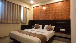 A hotel room with a large bed, a headboard with a patterned design, and a window with curtains. - Hotel Avadh Palace (Ahmedabad)