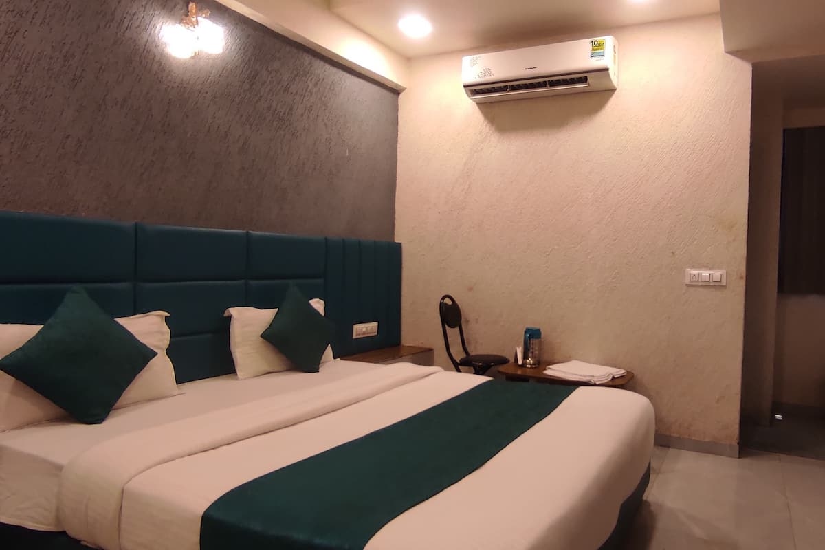 A hotel room with a large bed, a blue headboard, a flat-screen TV, an air conditioning unit, and a small desk with a lamp.