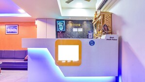 A reception desk with a digital screen, a sign for the reception, and a statue of a deity. - Hotel Avadh Palace (Ahmedabad)