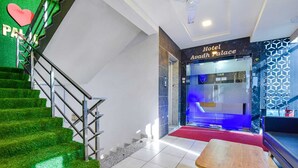A hotel lobby with a staircase, reception desk, and a red carpet leading to the entrance. - Hotel Avadh Palace (Ahmedabad)